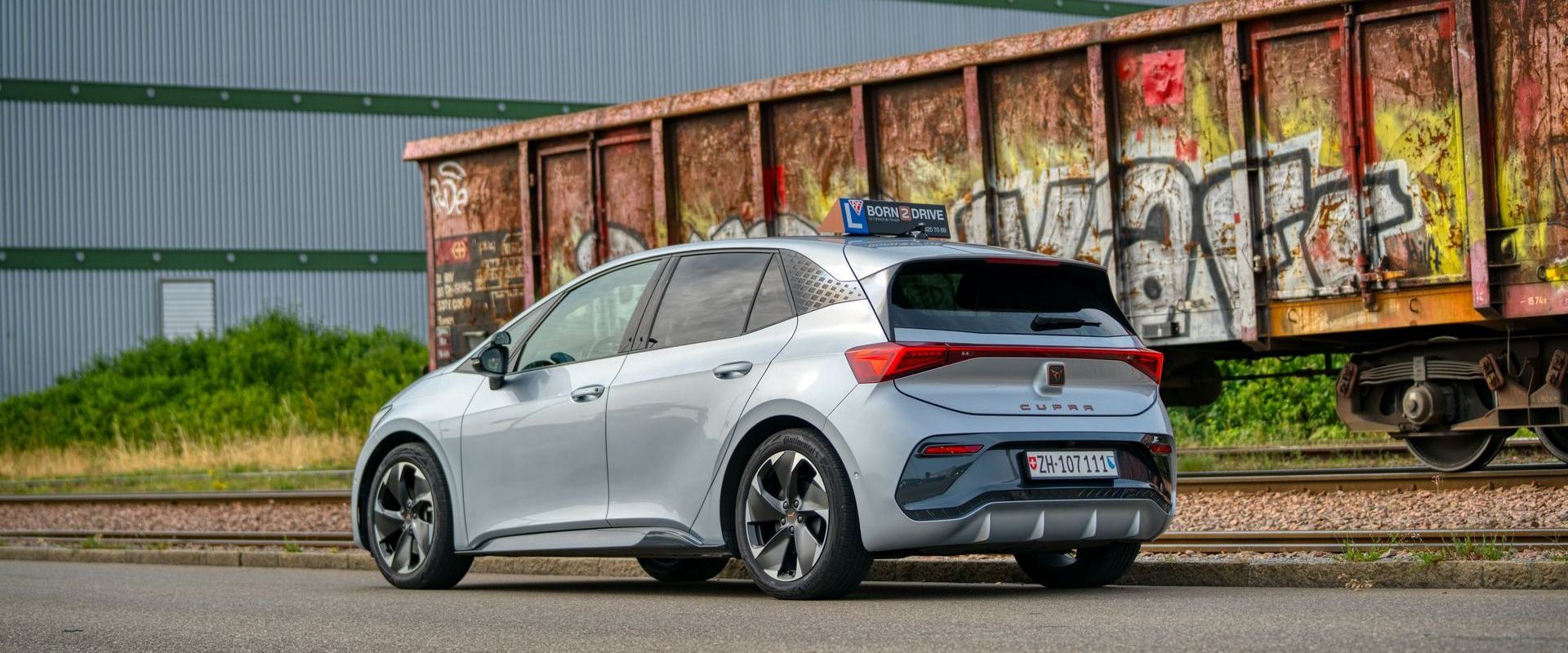 Vor einem Zugwaggon parkt ein silbernes Auto mit Graffiti darauf.