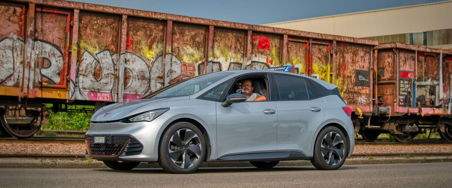 Cupra Born parkt vor einem Güterwagen mit Graffiti darauf.