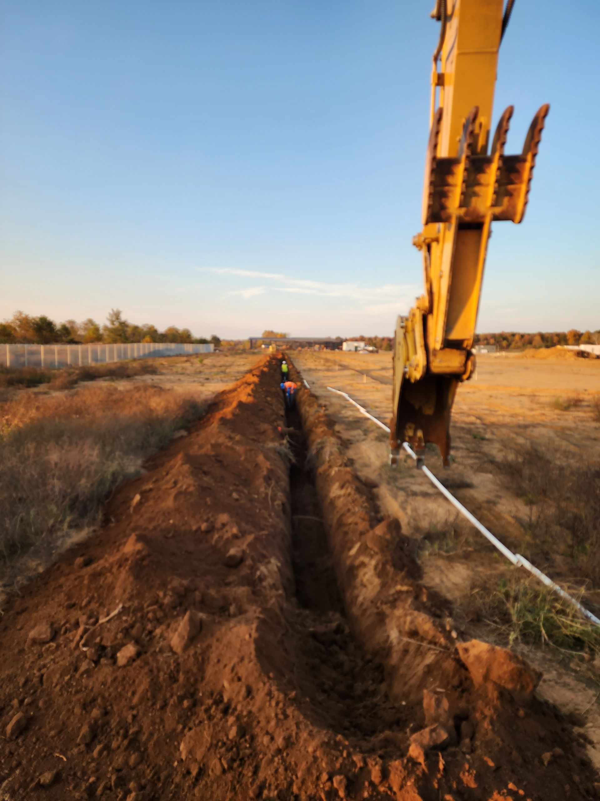 A yellow excavator is digging a trench in the dirt