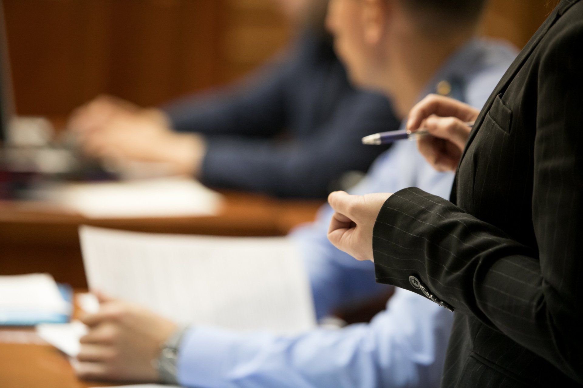 A woman is holding a pen while standing in front of a group of people.