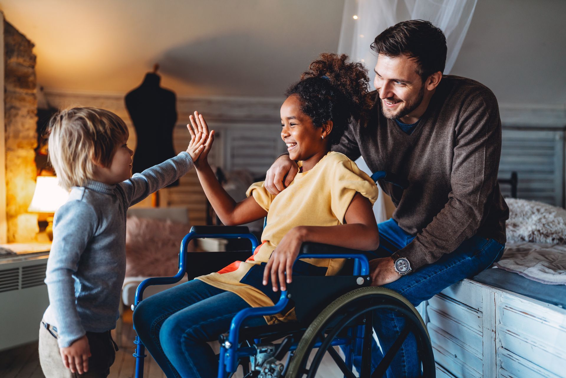 A little girl in a wheelchair is giving a high five to her father and brother.