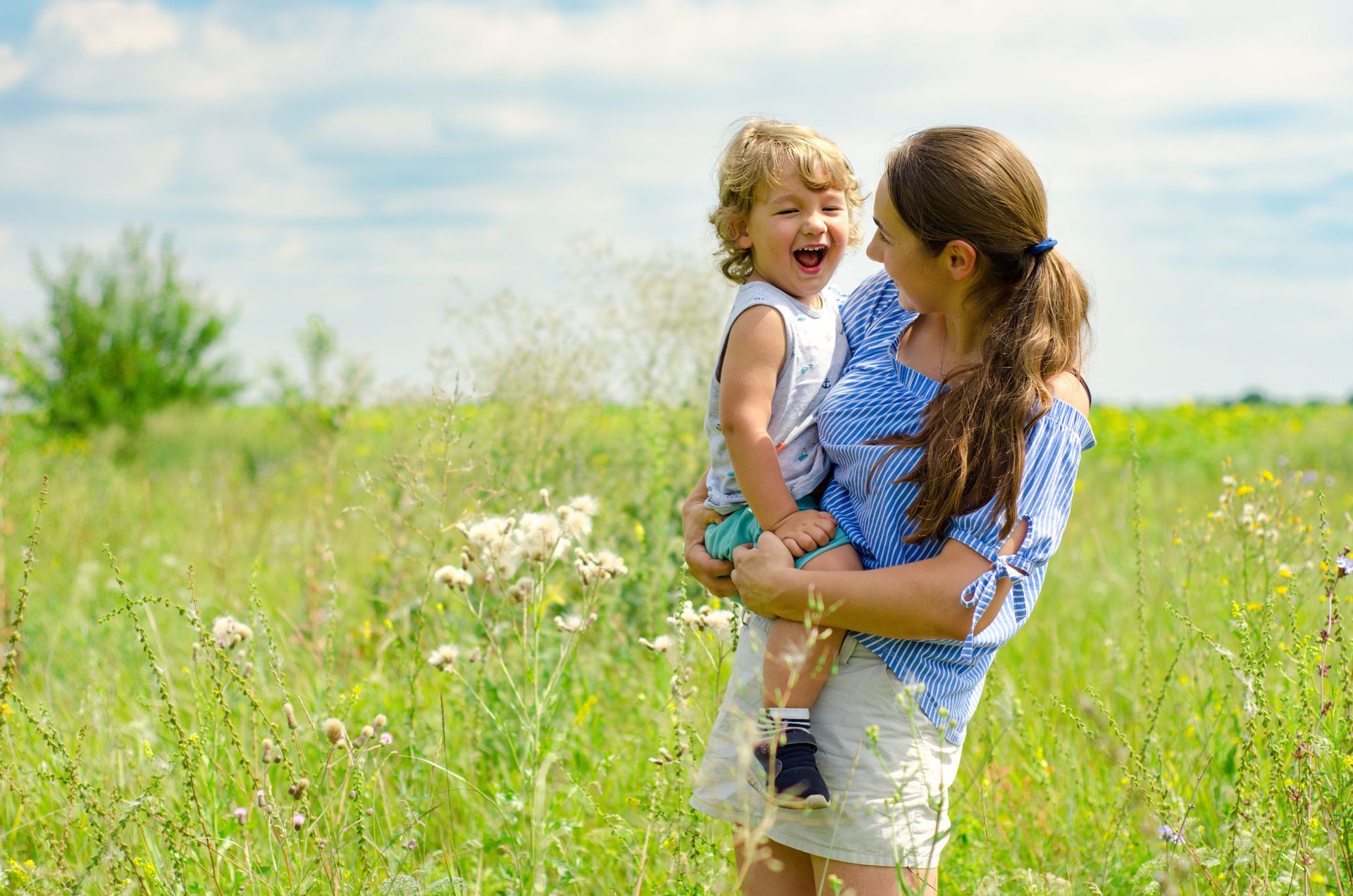 A woman and a child are laying under a blue blanket on a bed.