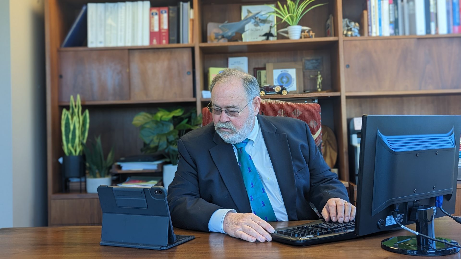 A man in a suit and tie is sitting at a desk using a computer.
