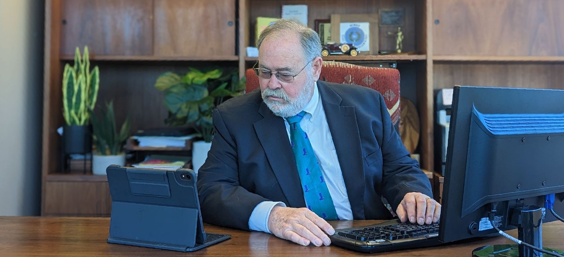A man in a suit and tie is sitting at a desk using a laptop computer.