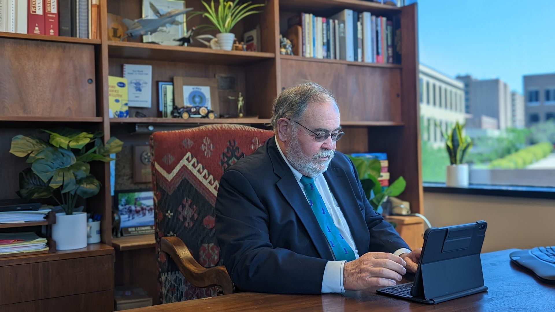 A man in a suit and tie is sitting at a desk using a tablet computer.