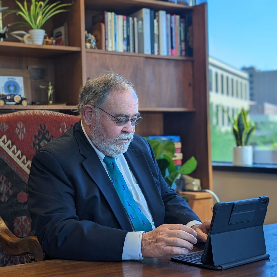 A man in a suit and tie is sitting at a desk using a tablet computer.