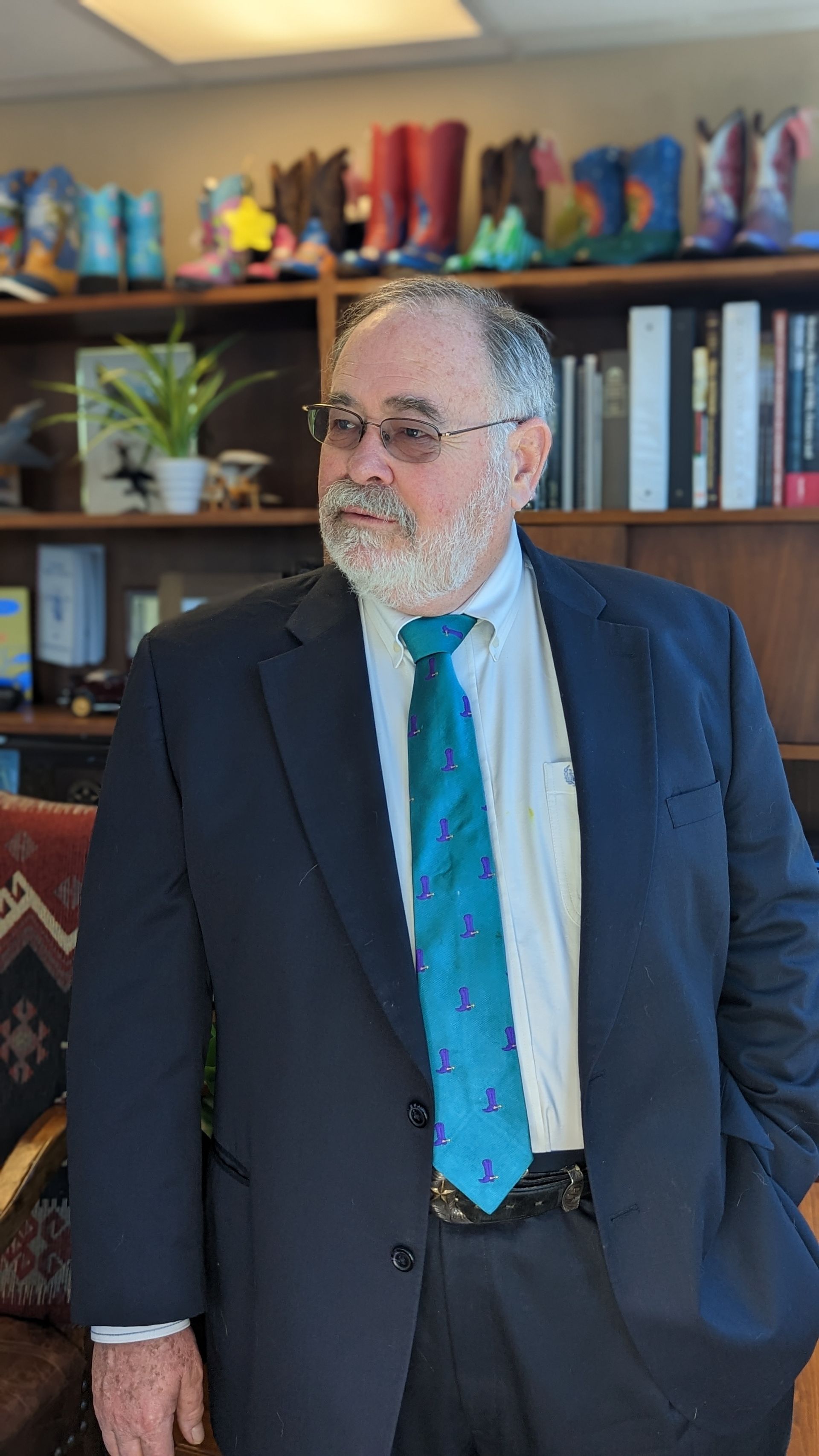 A man in a suit and tie is standing in front of a bookshelf.