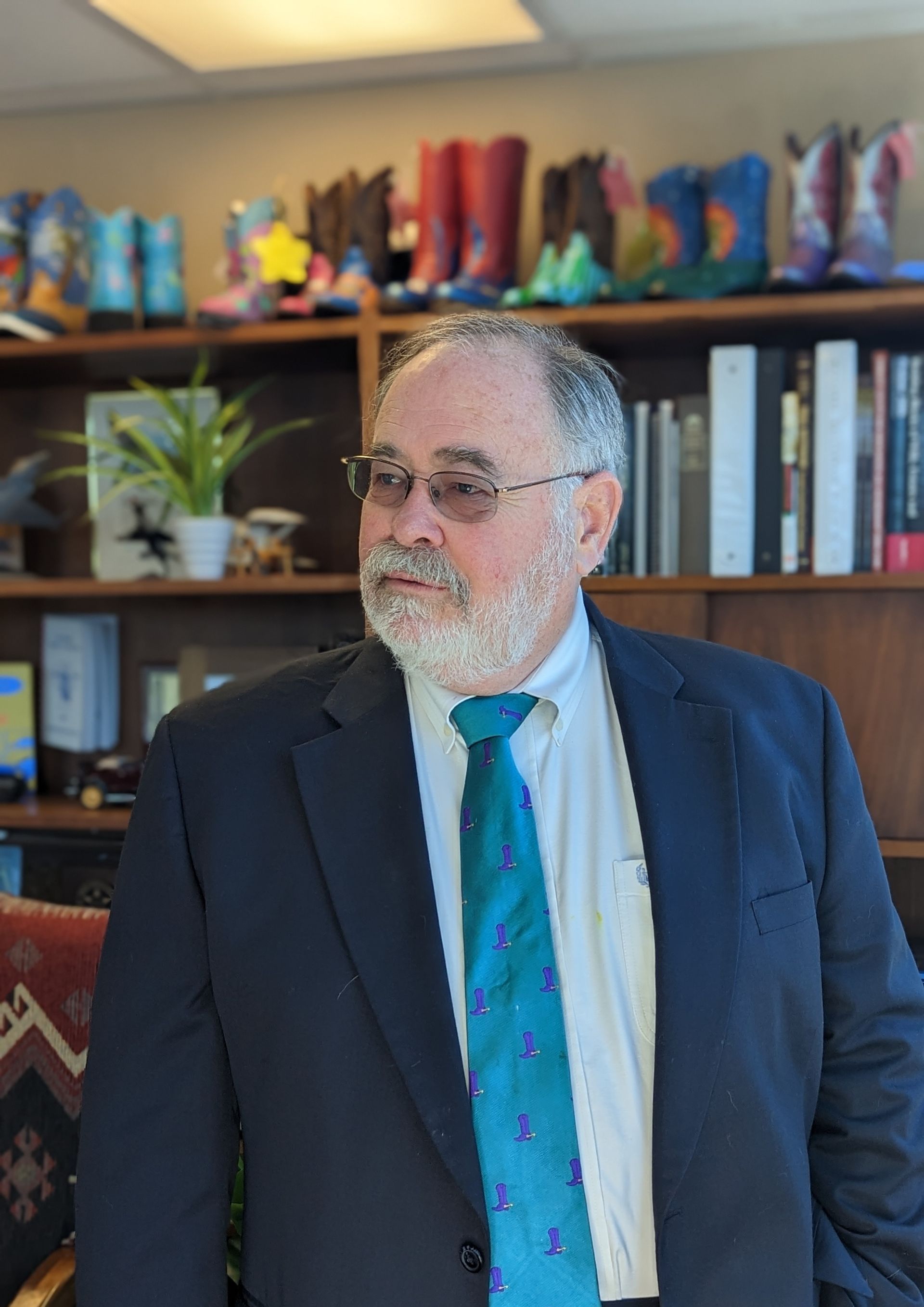 A man in a suit and tie is standing in front of a bookshelf.
