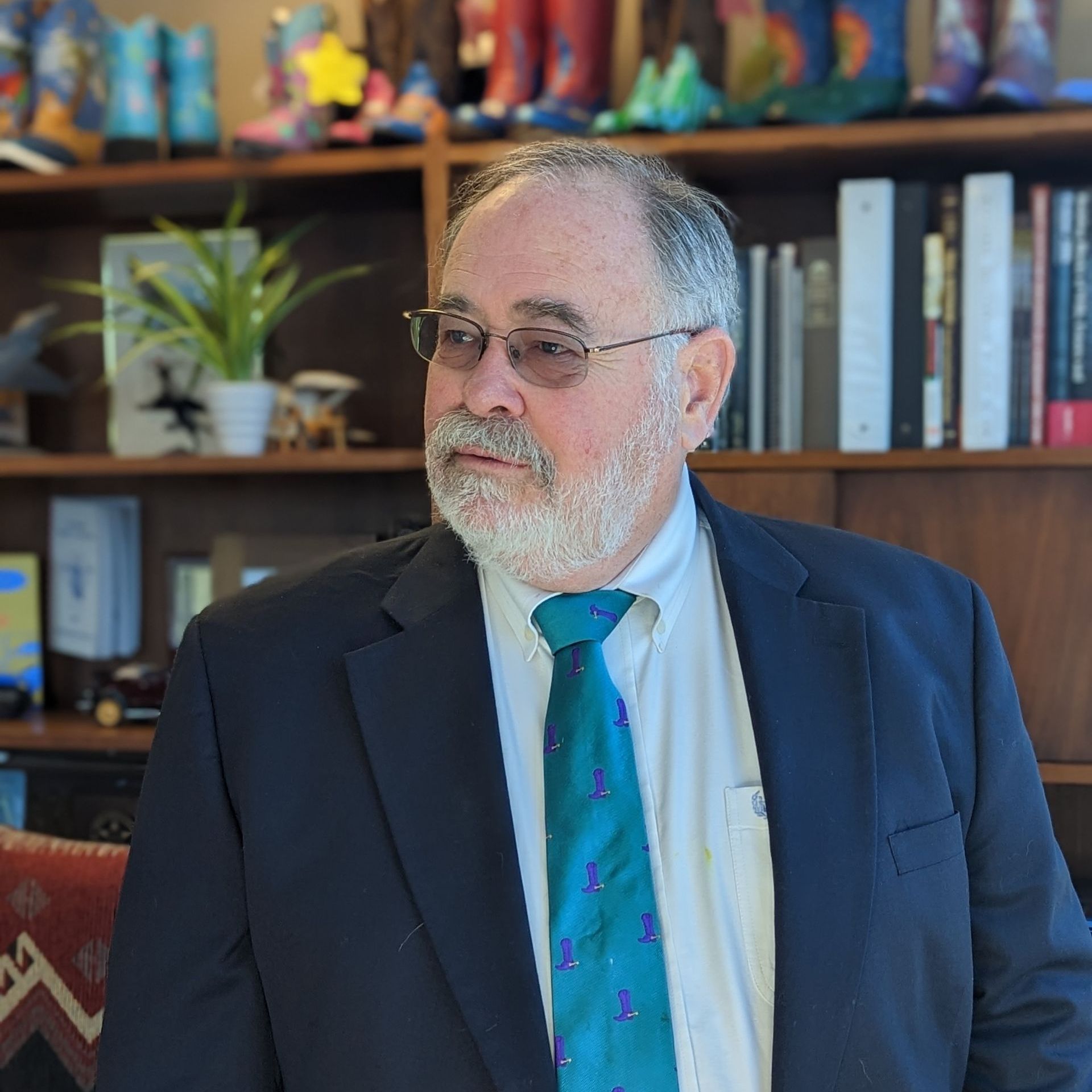 A man in a suit and tie is standing in front of a bookshelf.