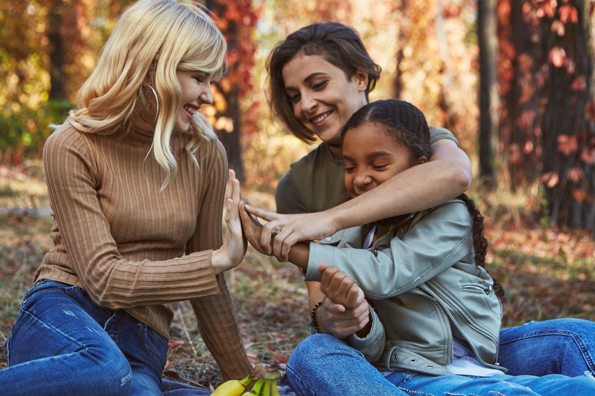 Three women and a child are sitting on a blanket in the woods.
