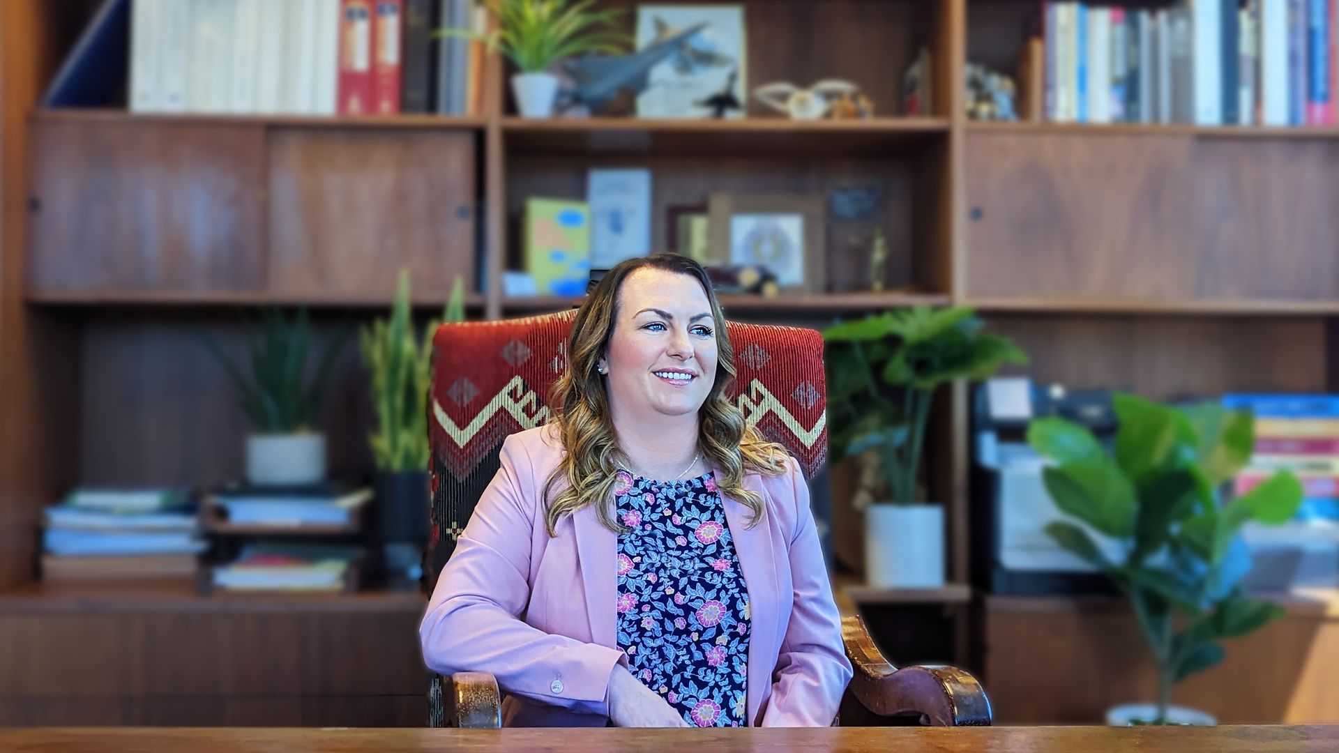 A woman is sitting at a desk in front of a bookshelf.
