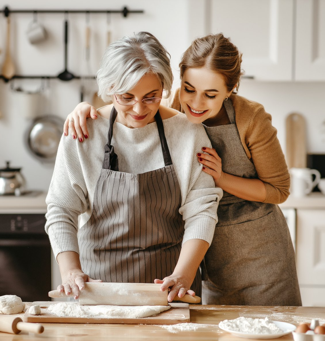 Two women are standing next to each other in a kitchen rolling dough.