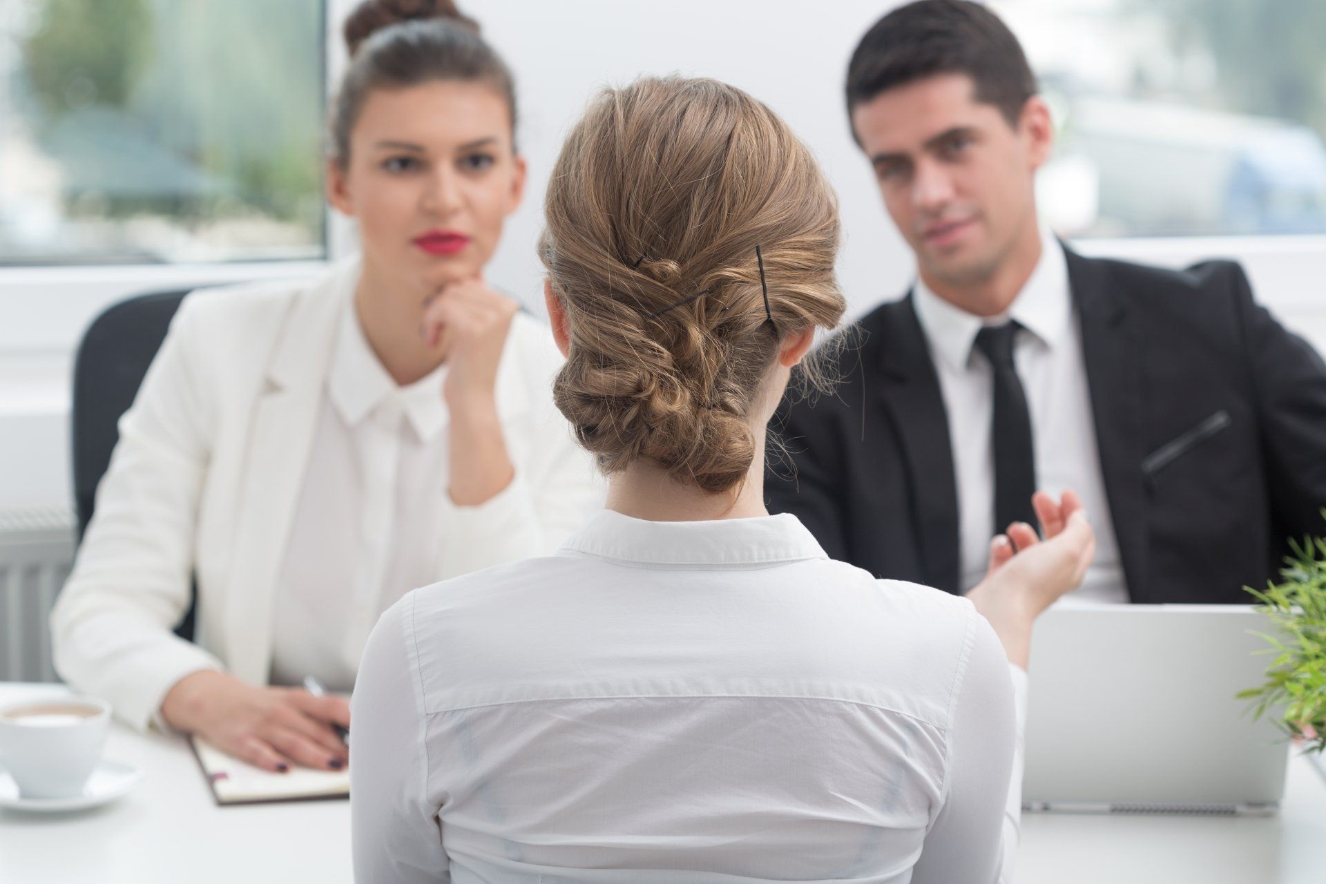 A woman is sitting at a table during a job interview while a man and woman look on.