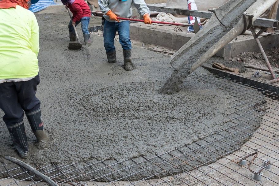 Workers pouring wet concrete from a mixer onto a road under construction