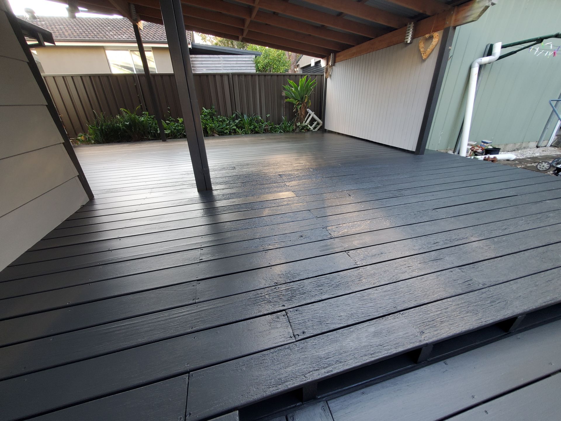 A black wooden deck with a fence in the background — JWP Painting & Property Services in Ettalong Beach, NSW