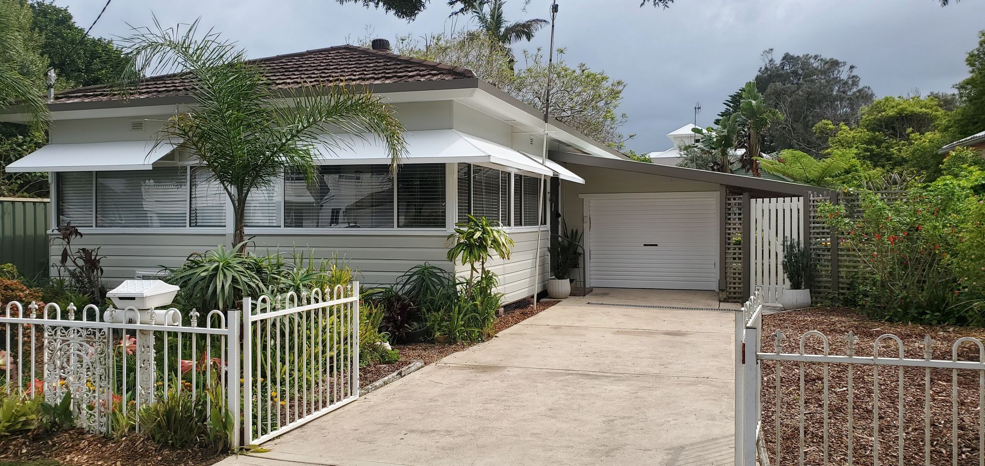 A white house with a white fence and a driveway leading to it — JWP Painting & Property Services in Ettalong Beach, NSW