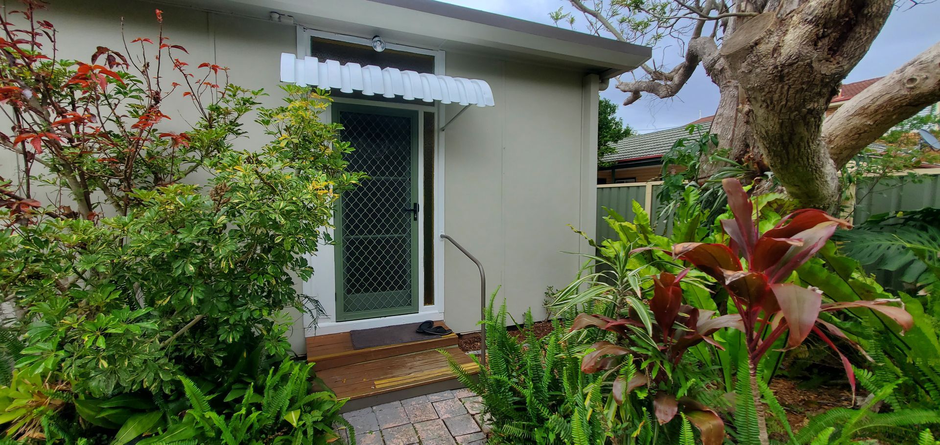 A small white house with a white awning over the door is surrounded by plants  and trees — JWP Painting & Property Services in Ettalong Beach, NSW