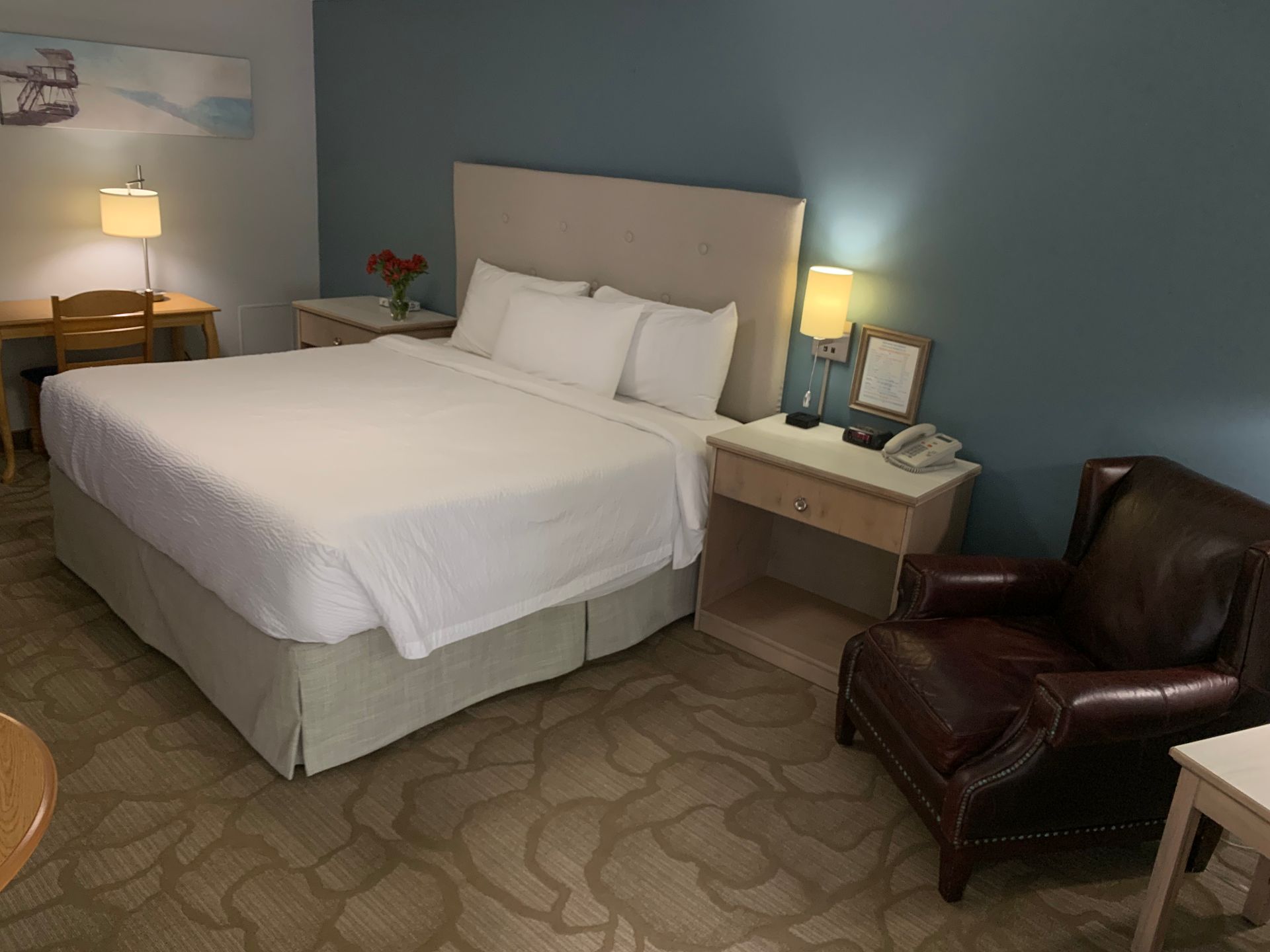 A hotel room with a king size bed , chair , desk and nightstand.