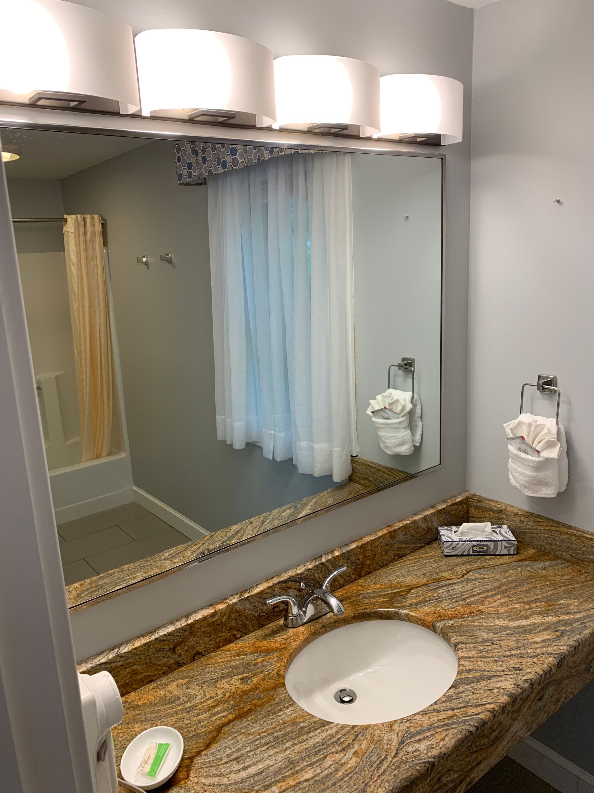 A bathroom with a sink , mirror and shower.