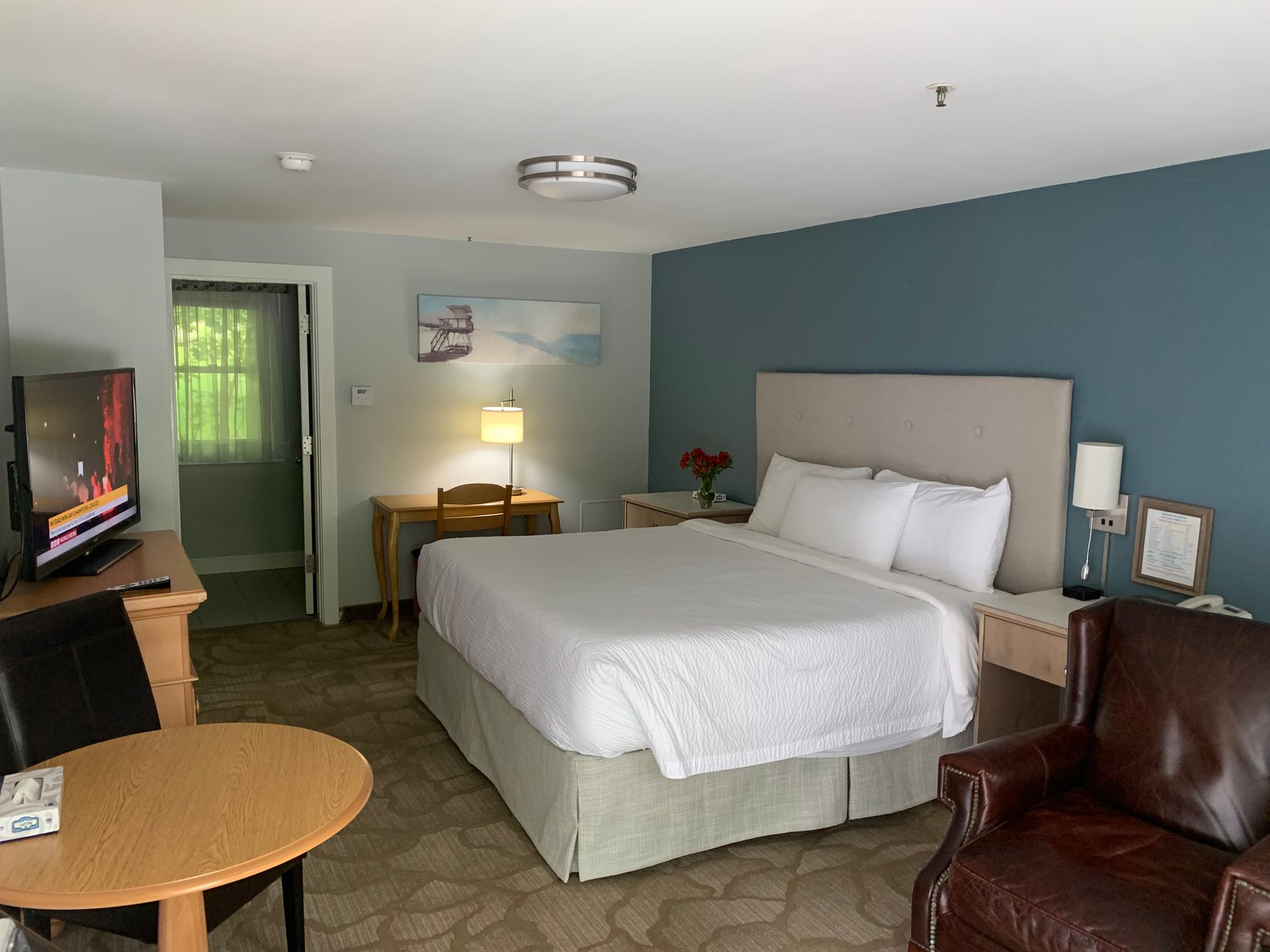 A hotel room with a king size bed , chair , table and television.