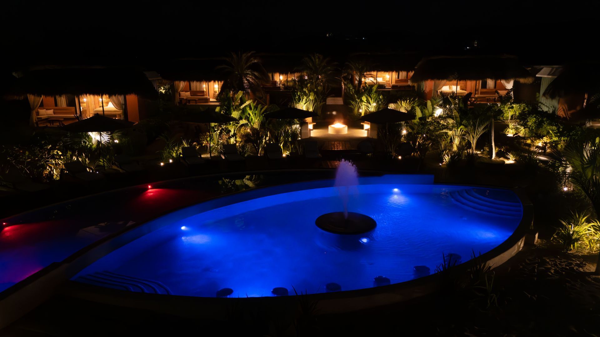 Una gran piscina con una fuente en el medio se ilumina por la noche.