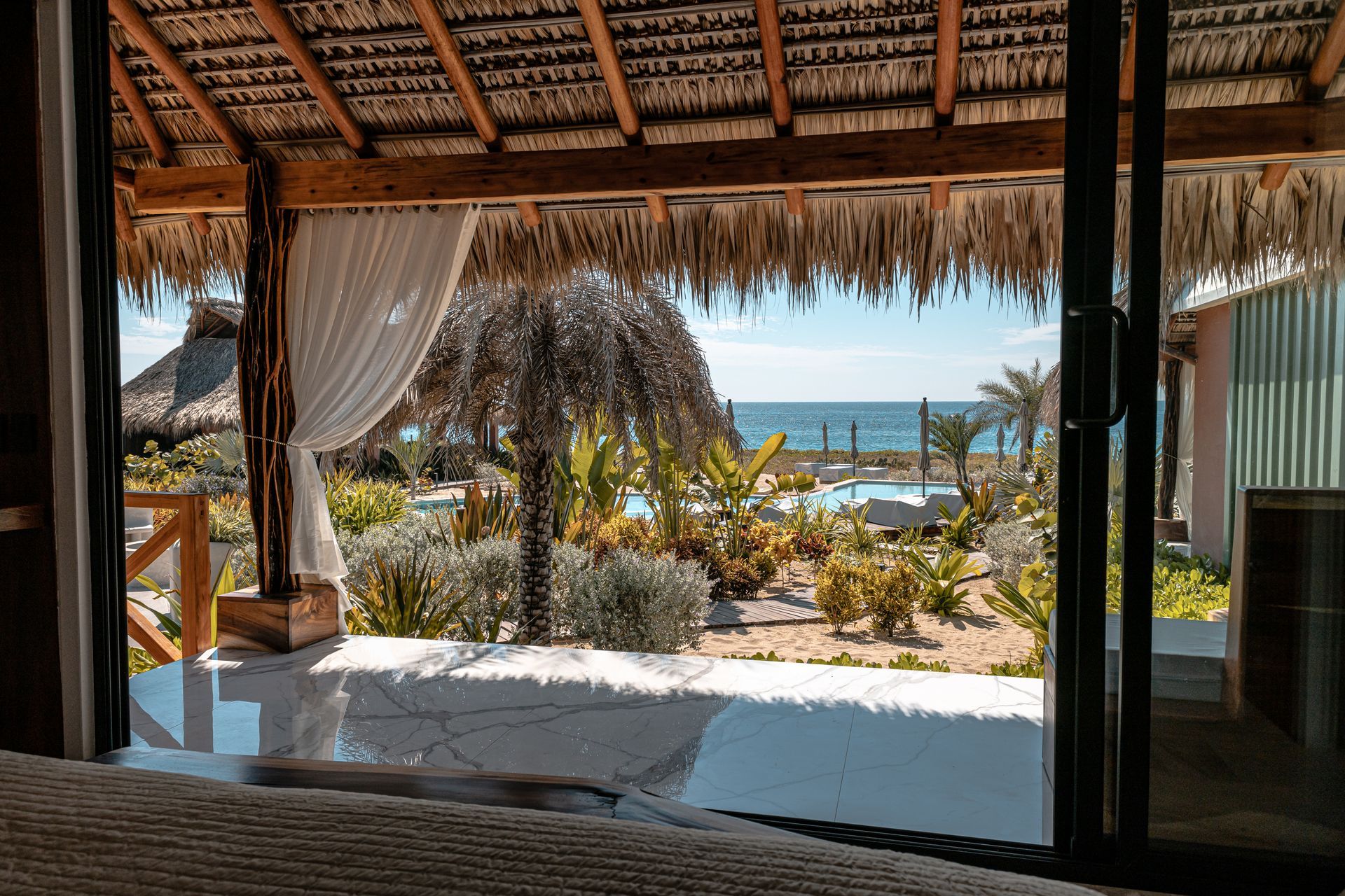 Una vista del océano desde una habitación de hotel con techo de paja.