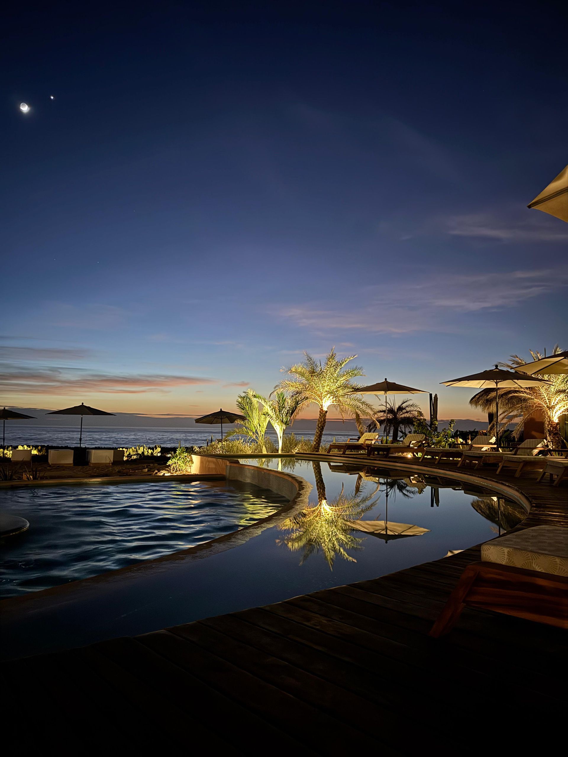 Una gran piscina rodeada de sombrillas y árboles por la noche.