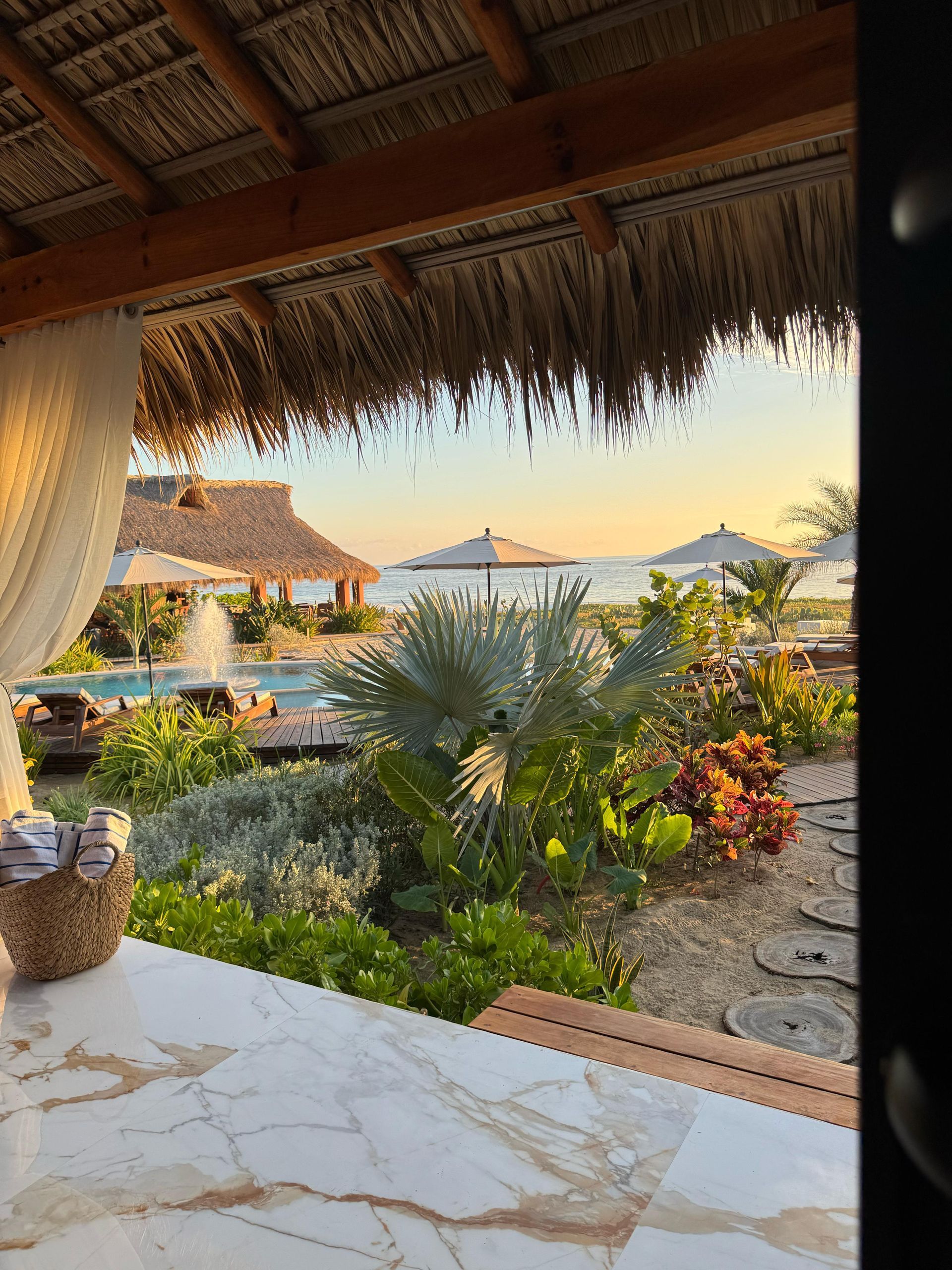 Un mirador con techo de paja con vistas a una piscina y una playa.