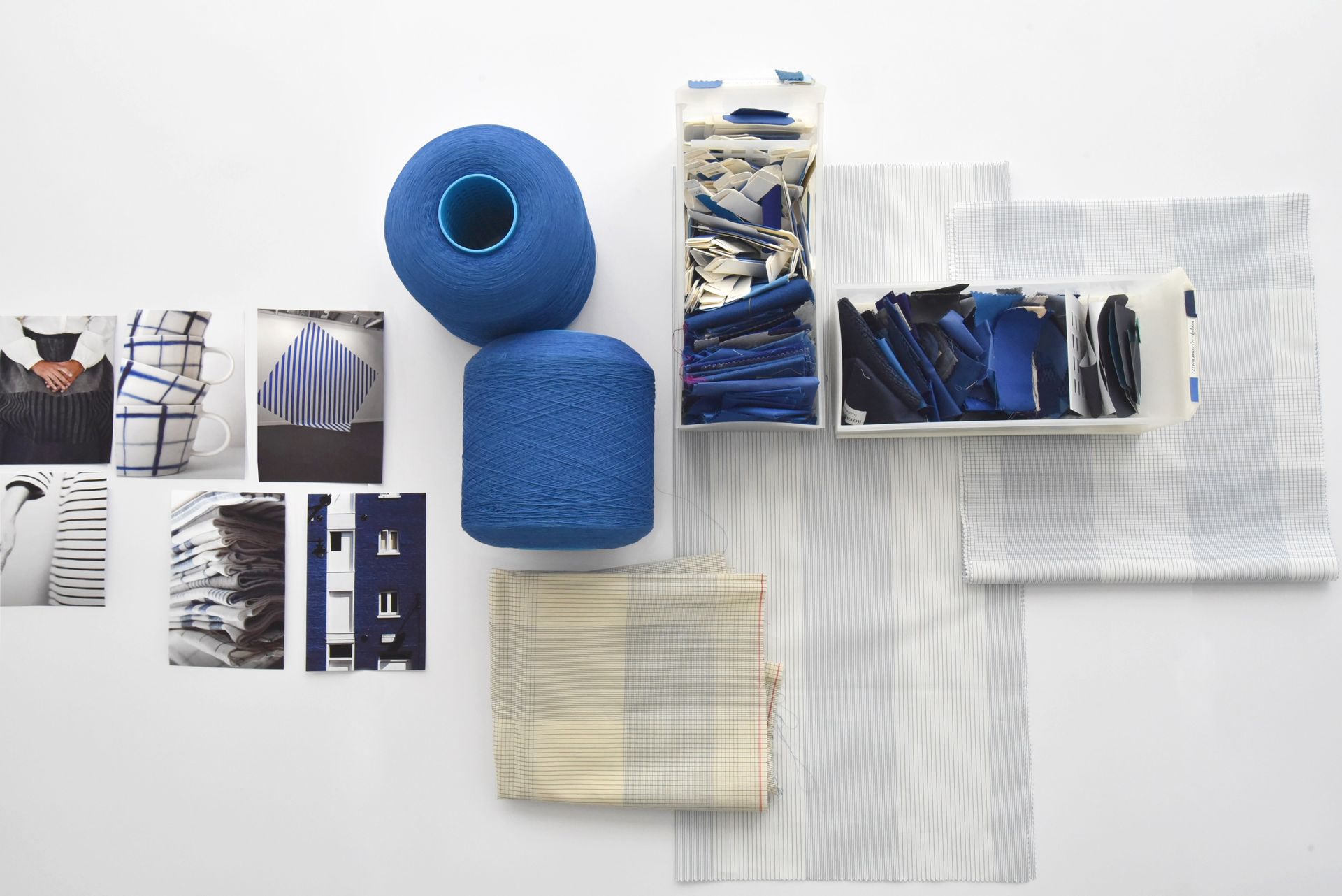 Assortment of blue yarn, fabric swatches, and small photographs arranged on a white surface.