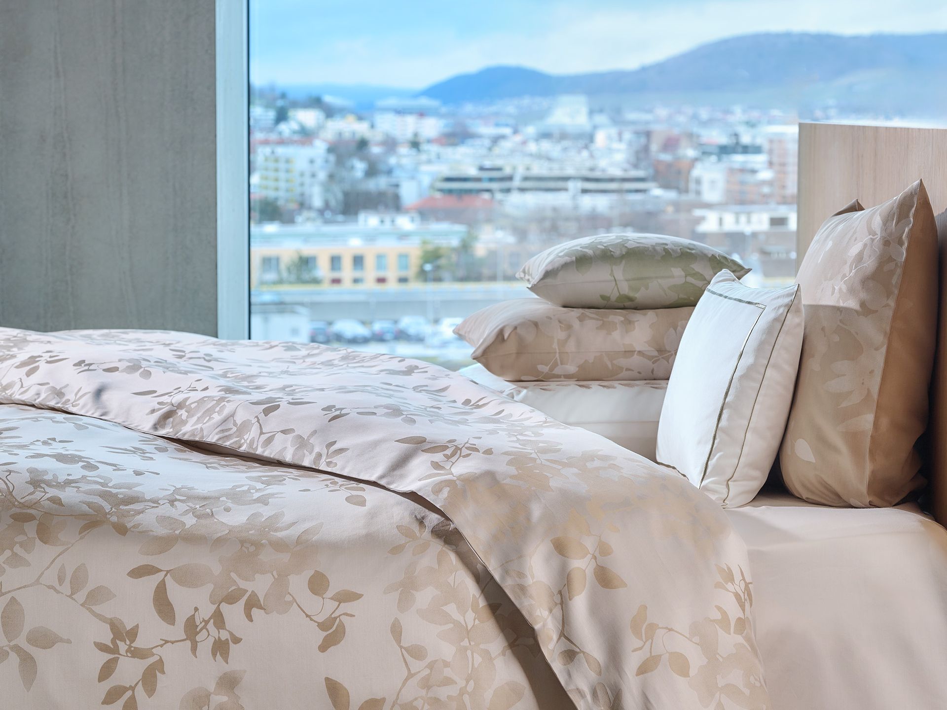 A woman in a bathrobe is sitting on a bed looking out a window.