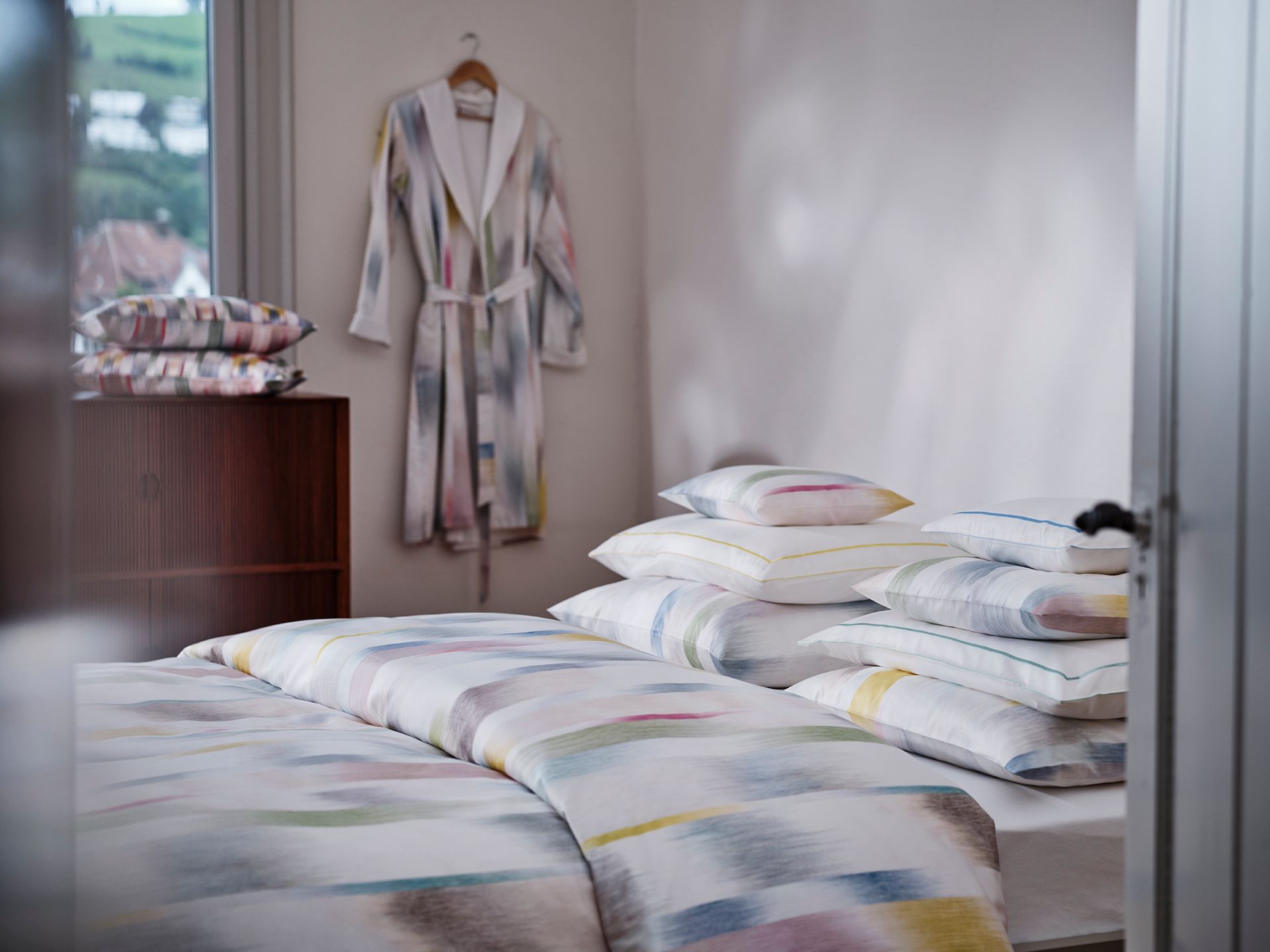 Bedroom with bed, pillows, patterned bedding, robe hanging on wall.