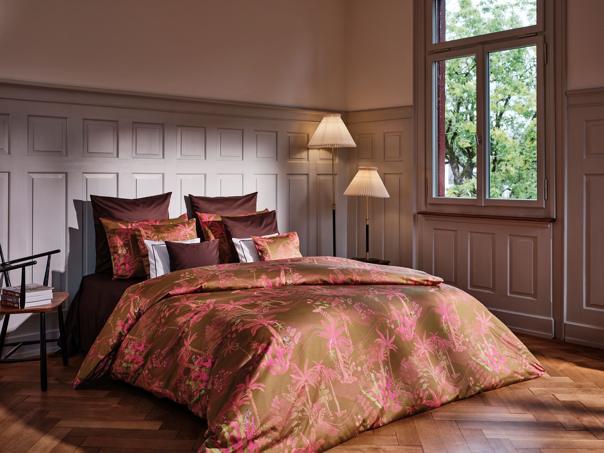 Bedroom with ornate bedspread featuring brown and pink floral pattern, paneled walls, and large window.
