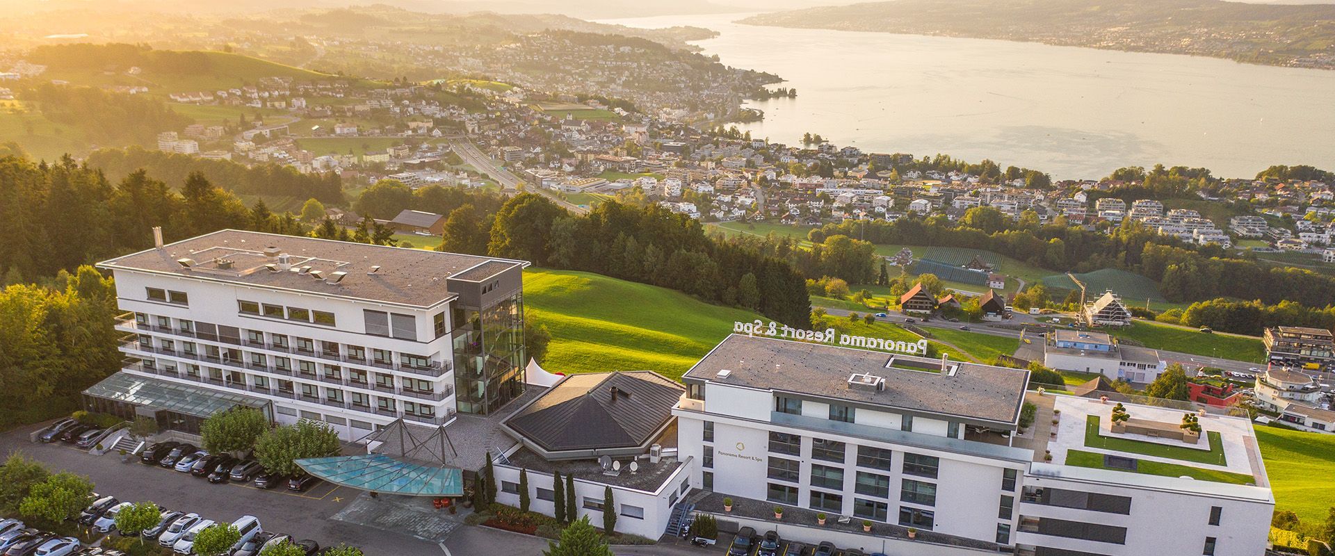 Aerial view of two white buildings with a cityscape and body of water in the background.