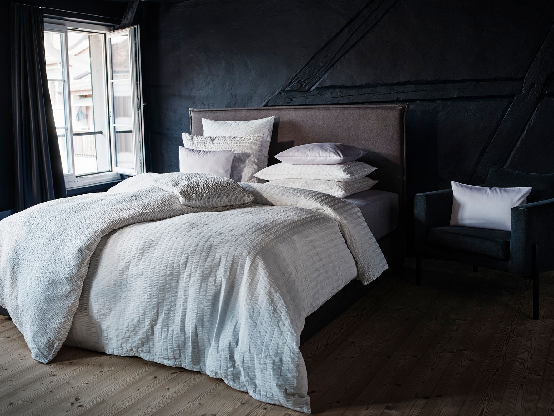 A bed with white sheets and pillows in a dark room