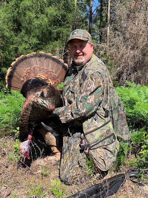 Camouflaged hunter kneels beside a wild turkey in a wooded clearing