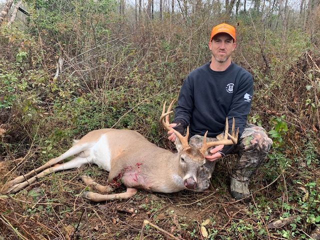 Hunter posing with a deer he has harvested in a wooded area.
