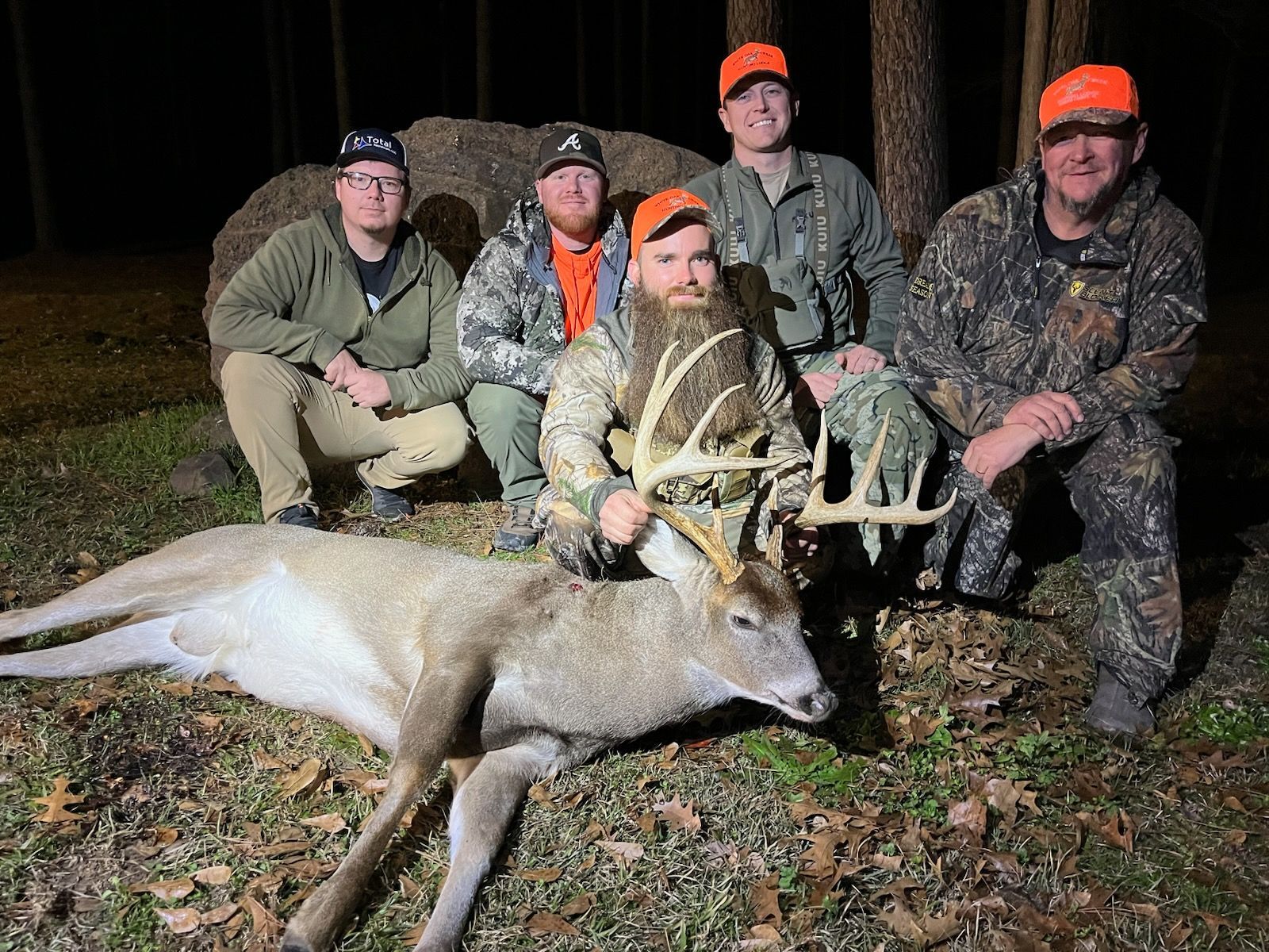 Five hunters posing with a large deer at night in the woods, one kneeling in front