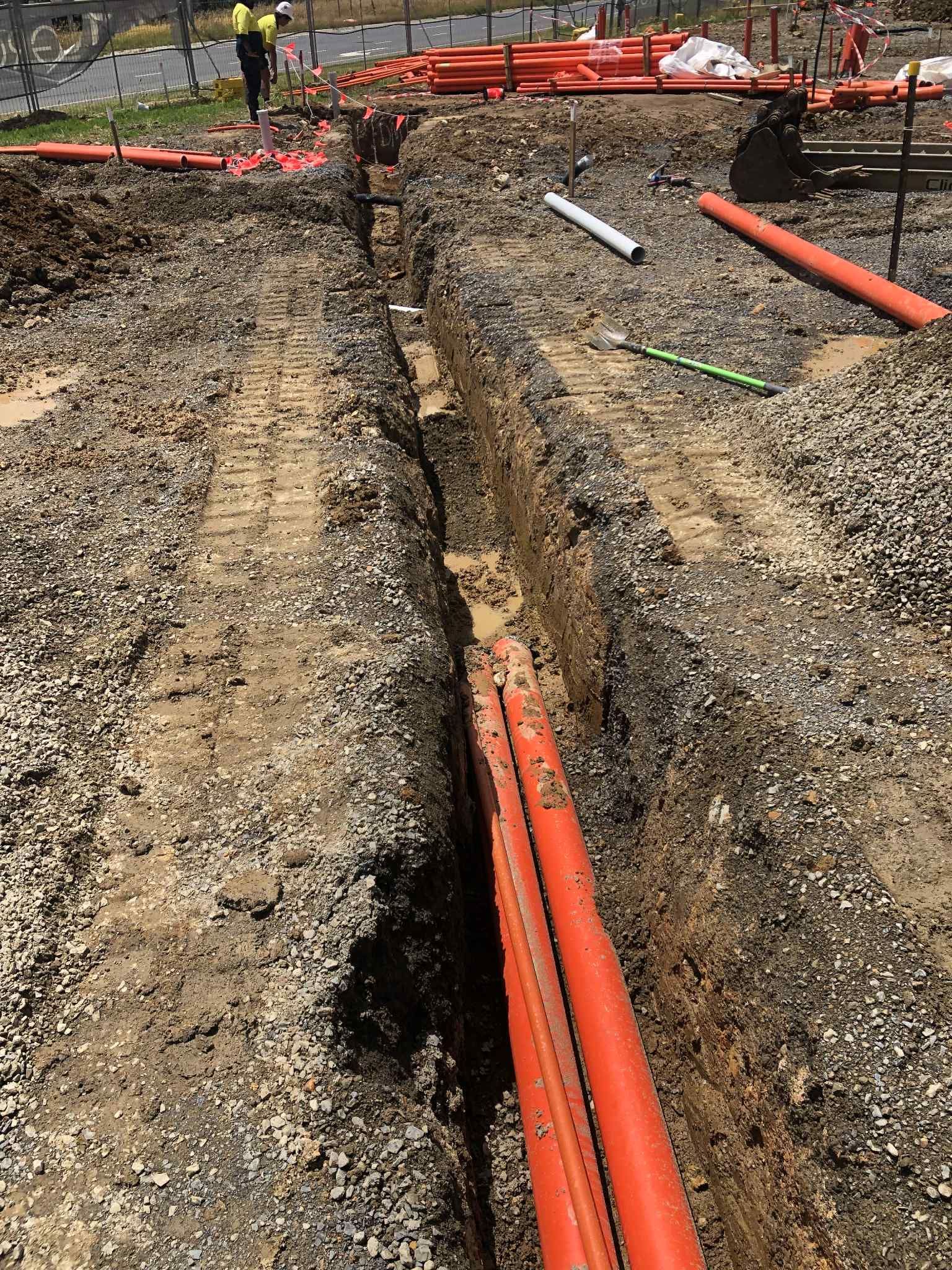 Underground electrical conduit trench with orange conduits laid for power cabling in Melbourne.
