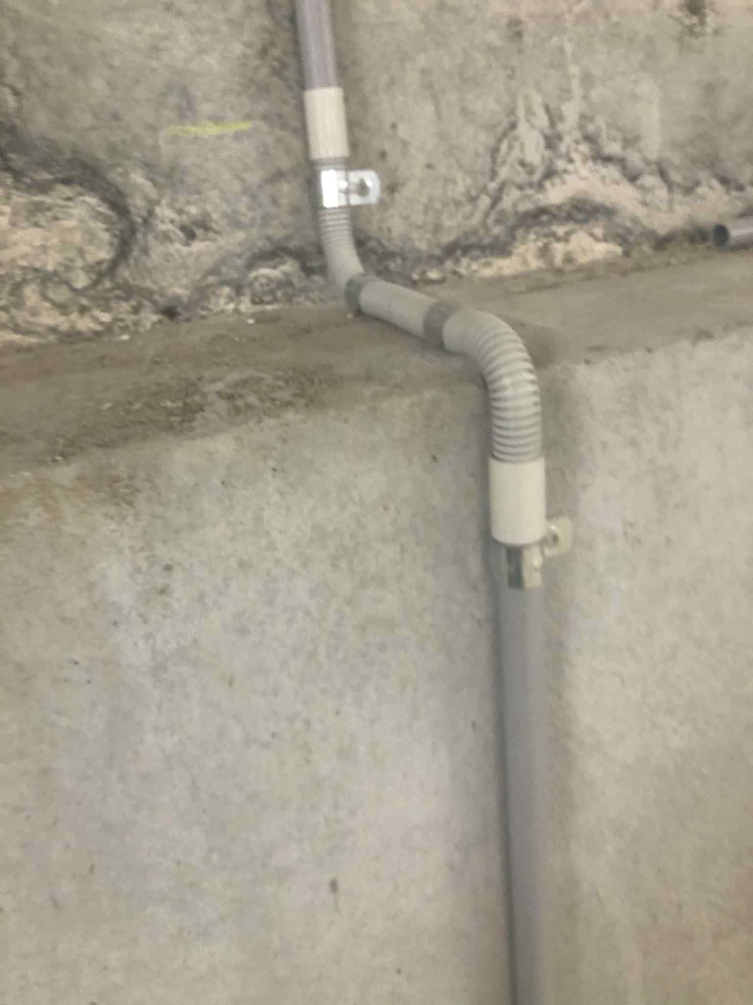 Ziesing Electrical: Flexible conduit clipped to a rendered concrete wall protecting cable run during outdoor electrical work.