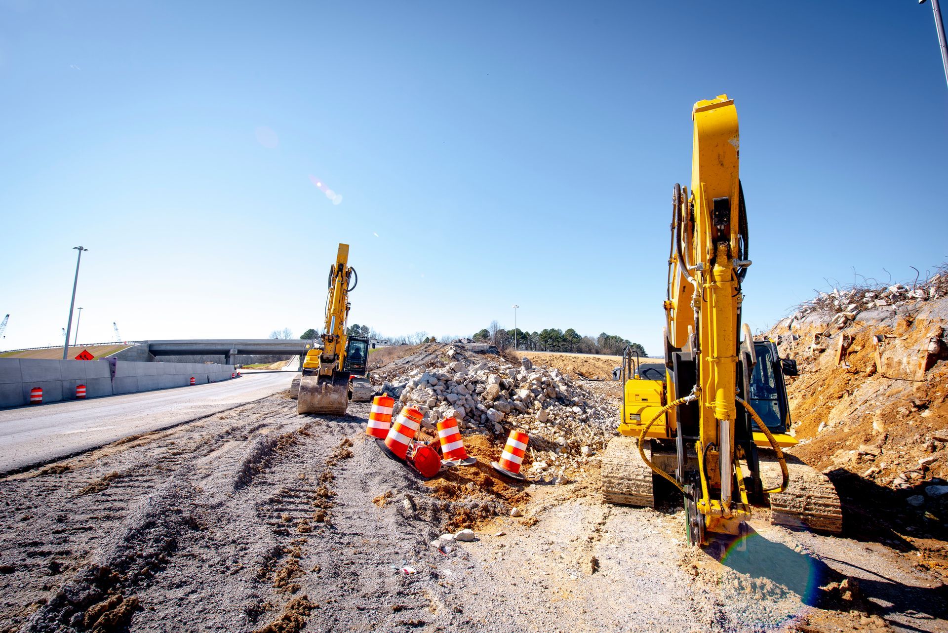 Two yellow excavators at a construction site, orange cones, blue sky, and piles of rock. Two yellow excavators at a construction site, orange cones, blue sky, and piles of rock.