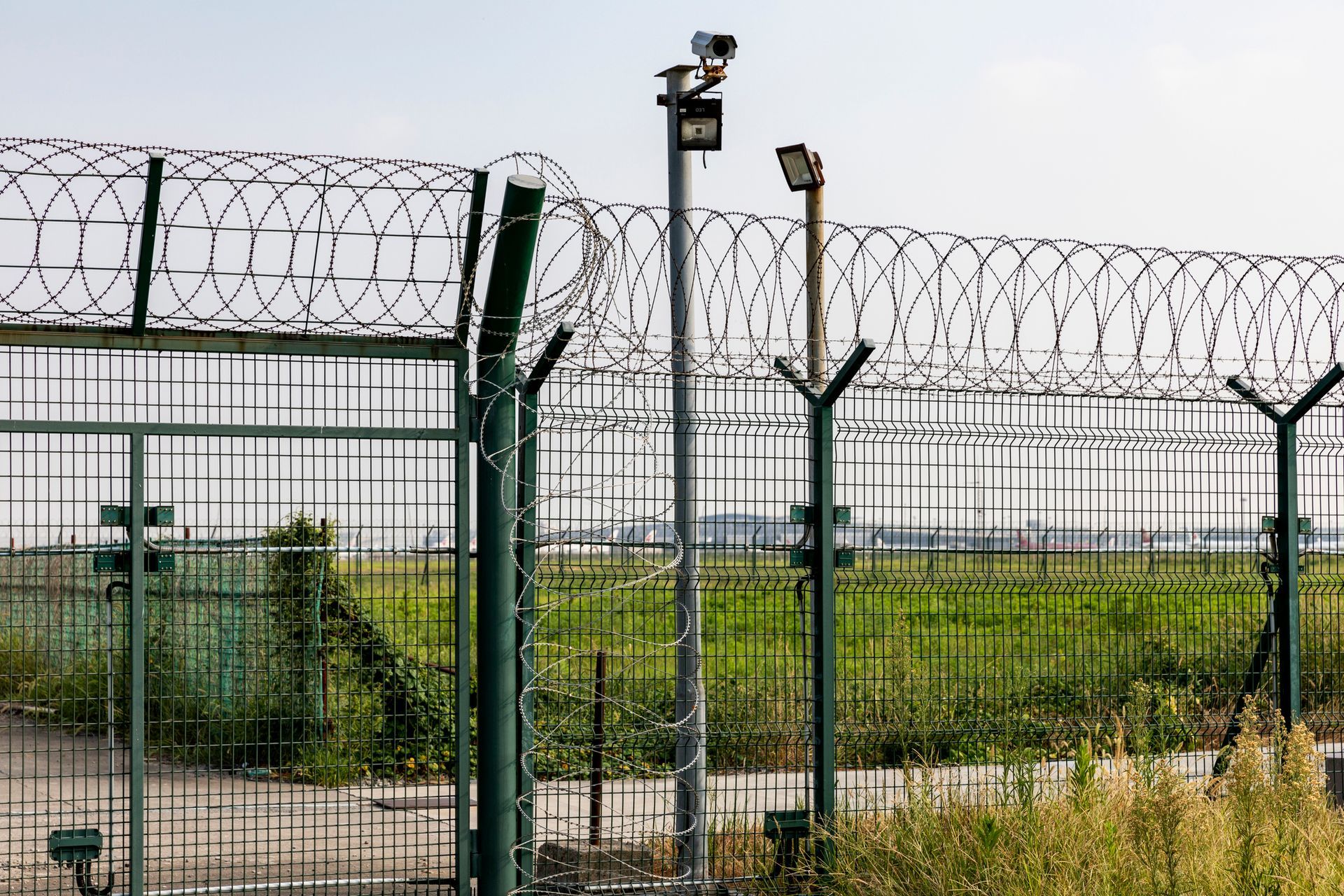 Security fence with razor wire, surveillance cameras, and field.