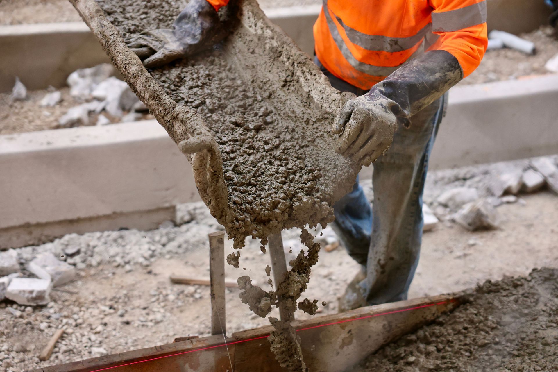 Worker pouring concrete from a wheelbarrow into a form. Orange vest, gloves, construction site. Worker pouring concrete from a wheelbarrow into a form. Orange vest, gloves, construction site.
