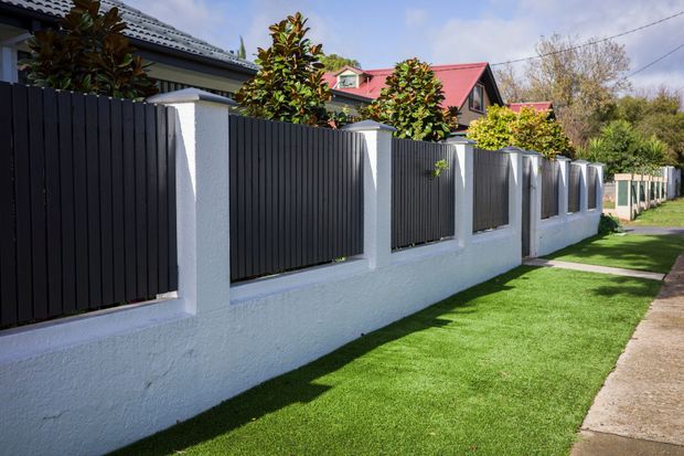 Black fence with white pillars and base, green lawn, residential setting.