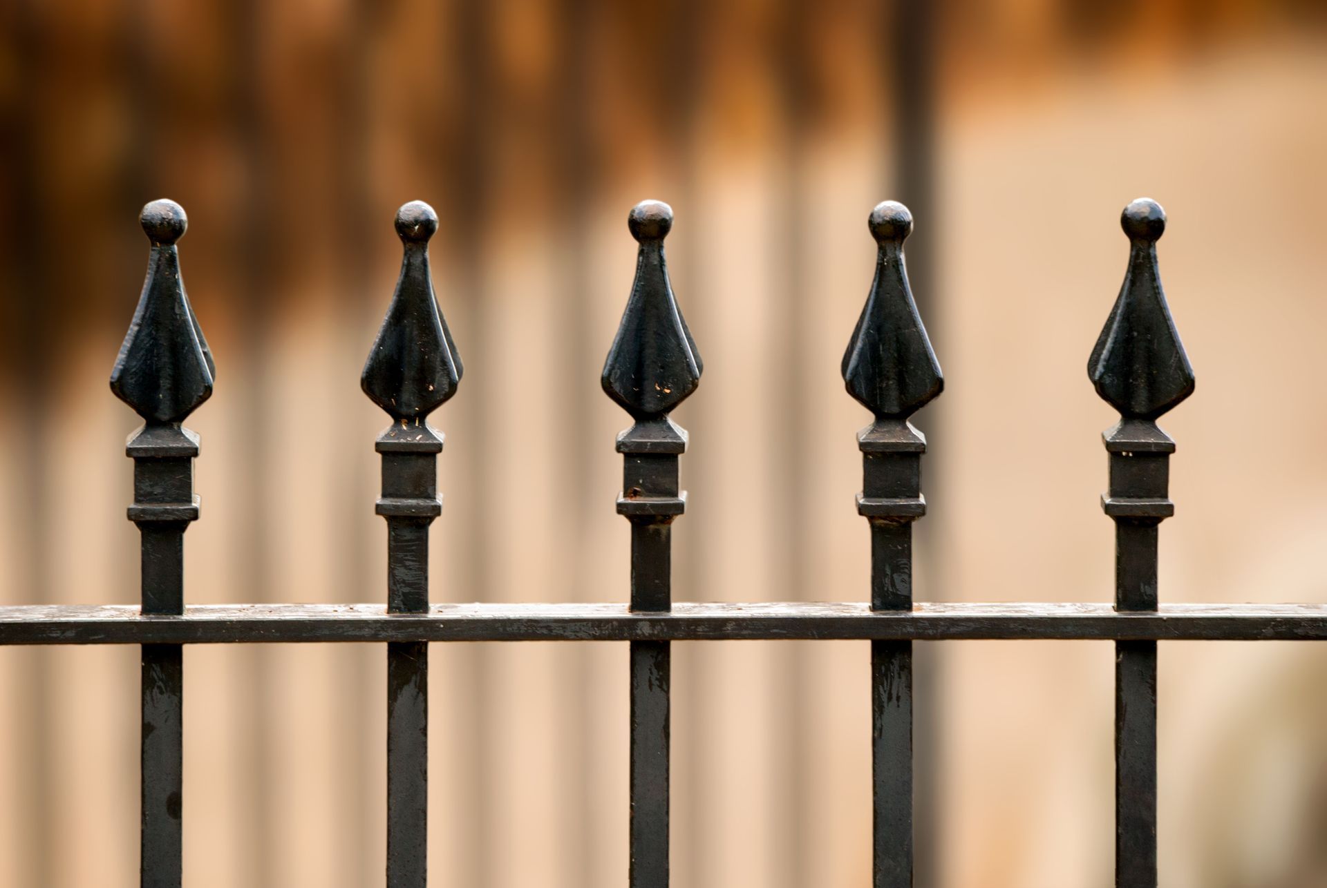 Black metal fence with spear-shaped tops against a blurred beige background.