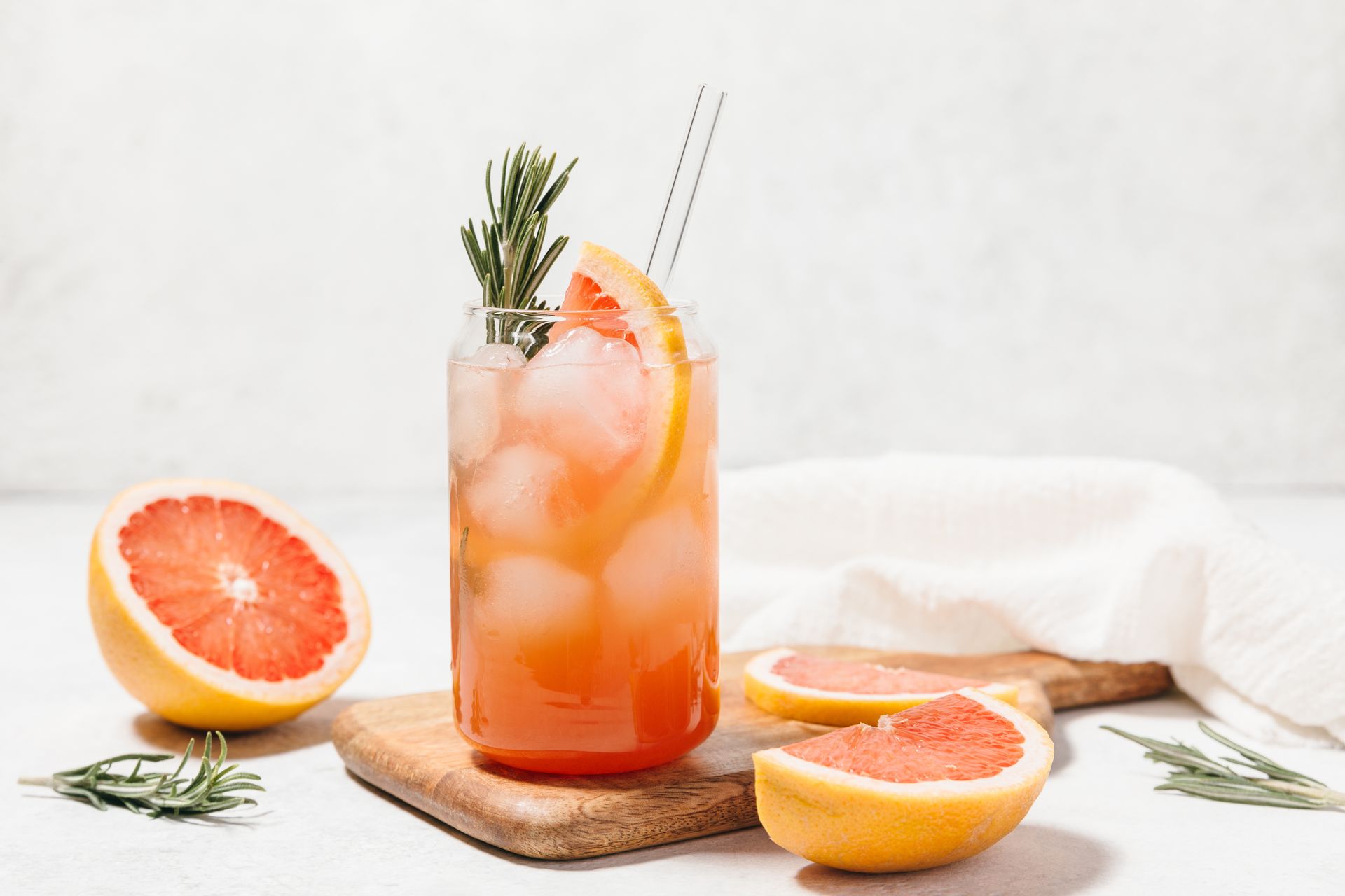 A glass of grapefruit juice with ice and a straw on a cutting board.