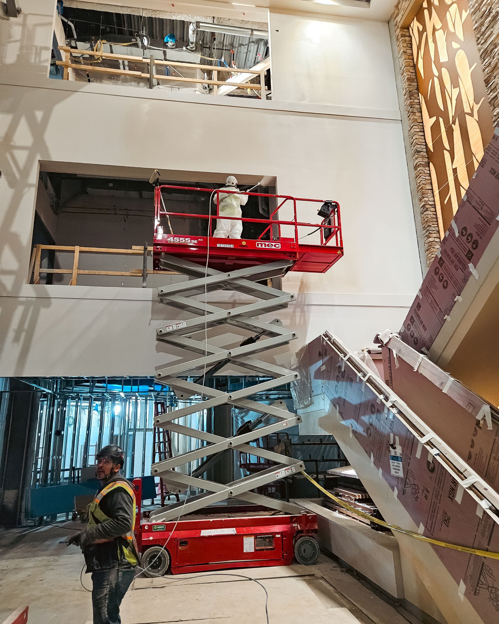 A man is standing next to a scissor lift in a building under construction.