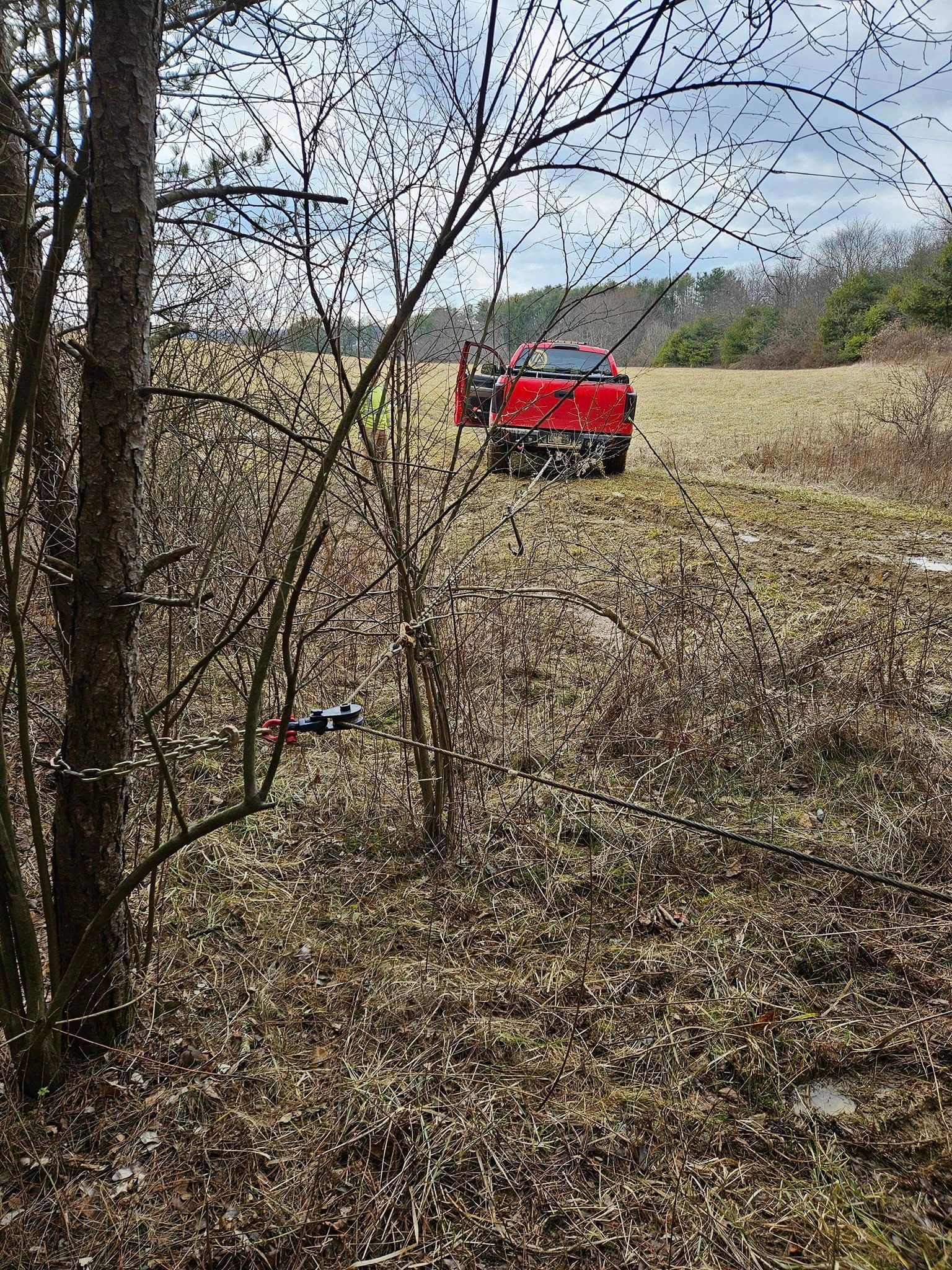 Red pickup truck in a field, with trees in the foreground. Door is open.