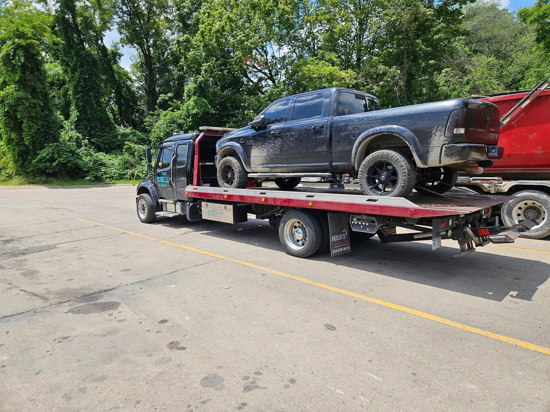 Black pickup truck loaded on a flatbed tow truck on a paved lot.