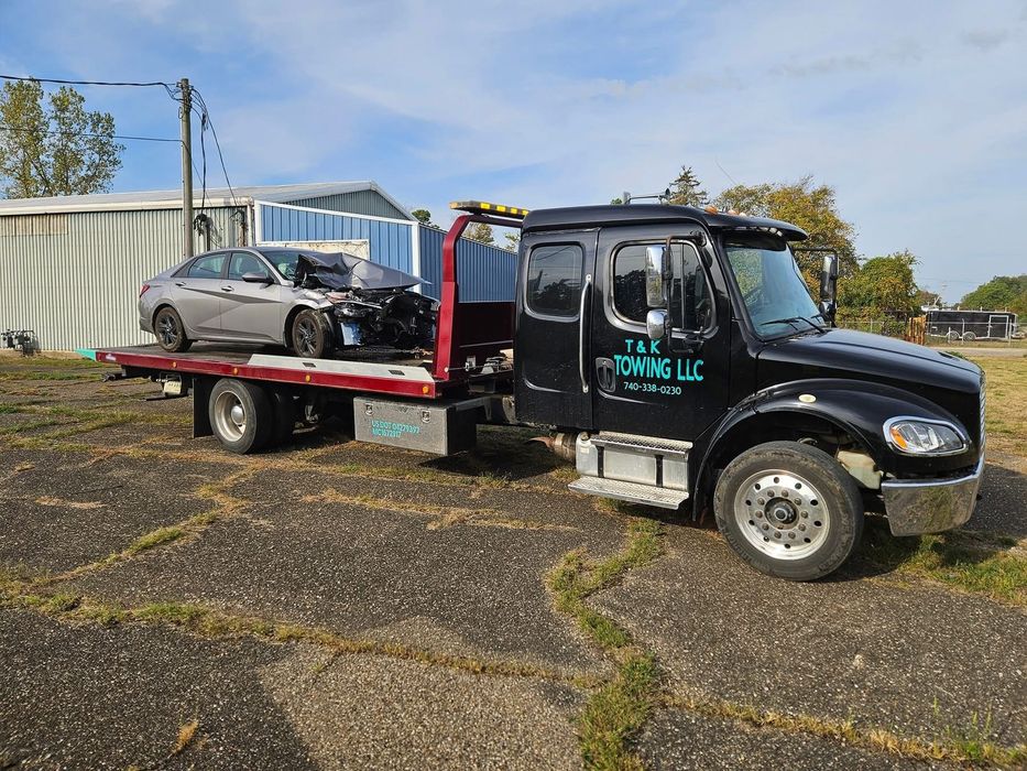 Tow truck carrying a heavily damaged gray sedan. The truck is black with