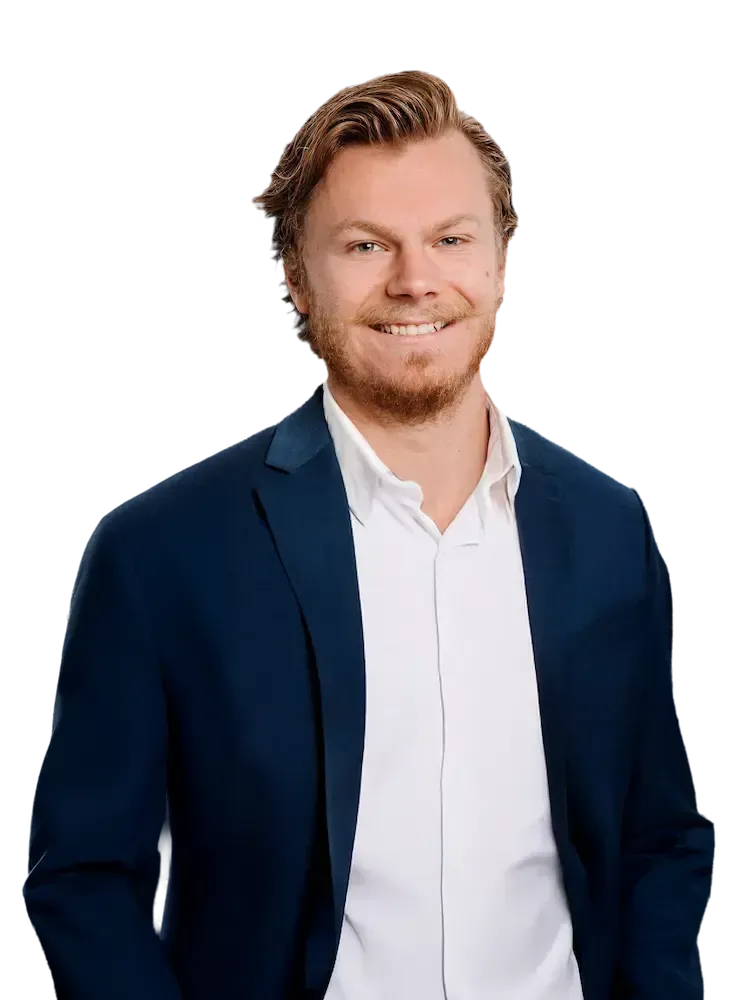 Sam Ivey in a suit smiles, looking at the viewer. He has a beard and is against a transparent background.